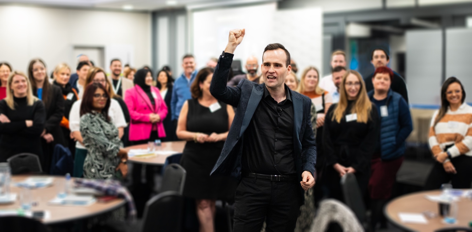 Andrew Ramsden on the floor of a packed forum room, arm raised, the audience standing with him